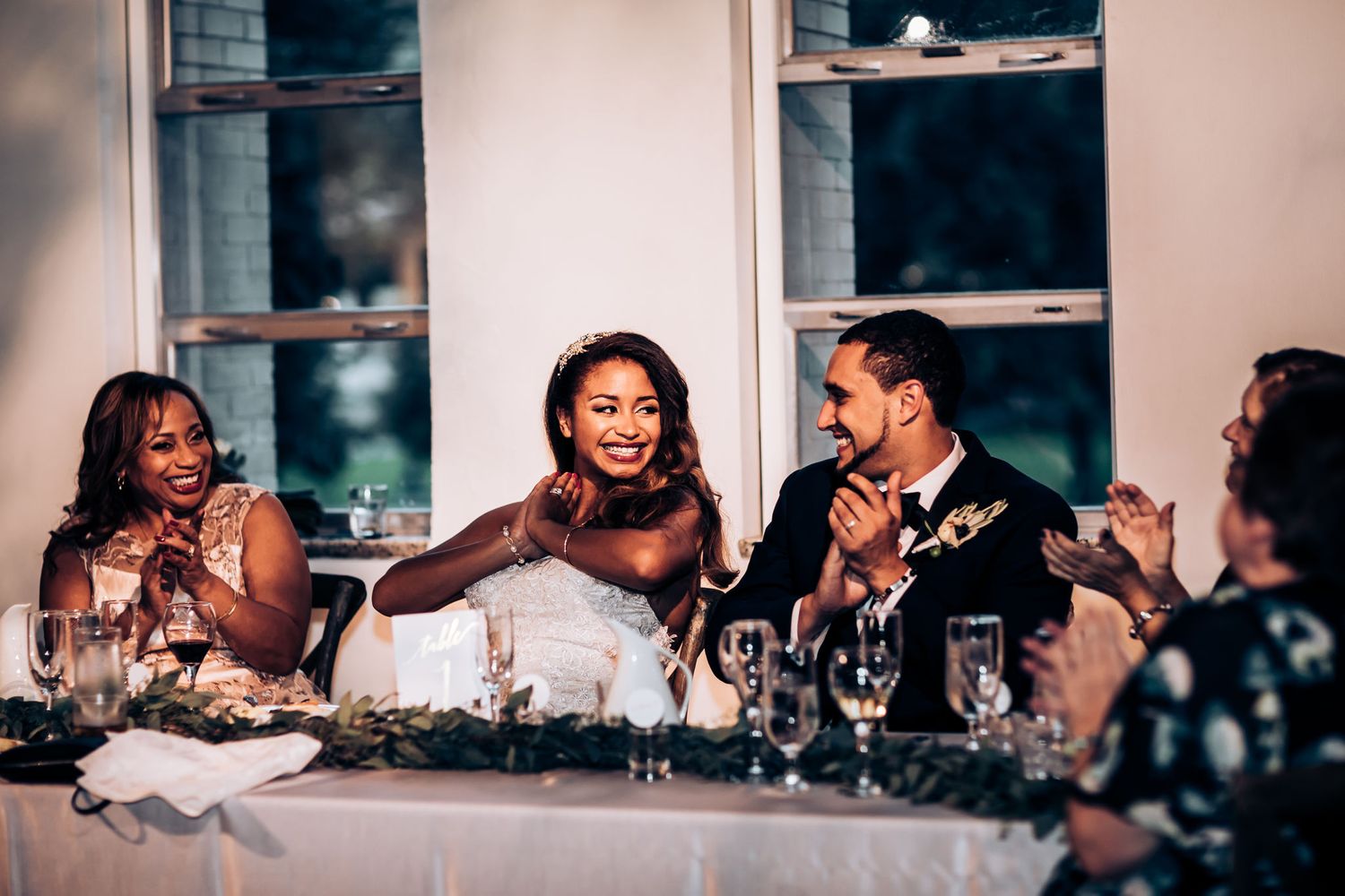 Wedding party seated at elegant head table sharing laughter during reception.