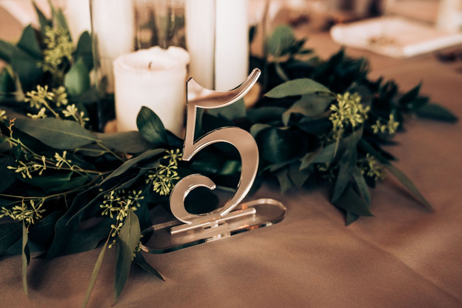 Wedding table number five surrounded by greenery and white candles.