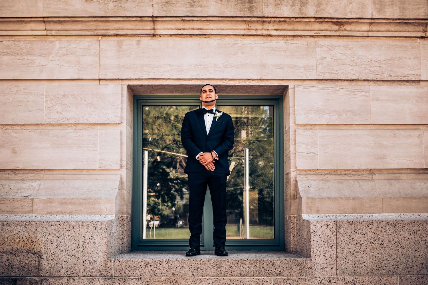 Groom in classic tuxedo stands formally in stone building archway.