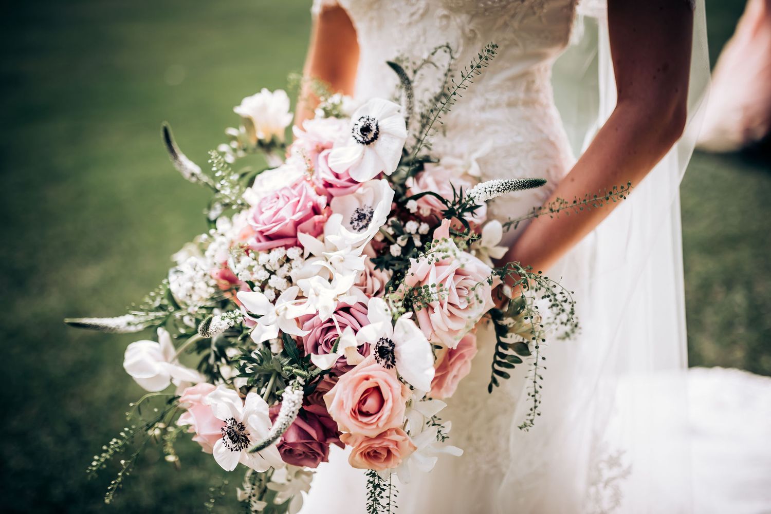 Close-up of romantic pink and white wedding bouquet with roses and delicate greenery.