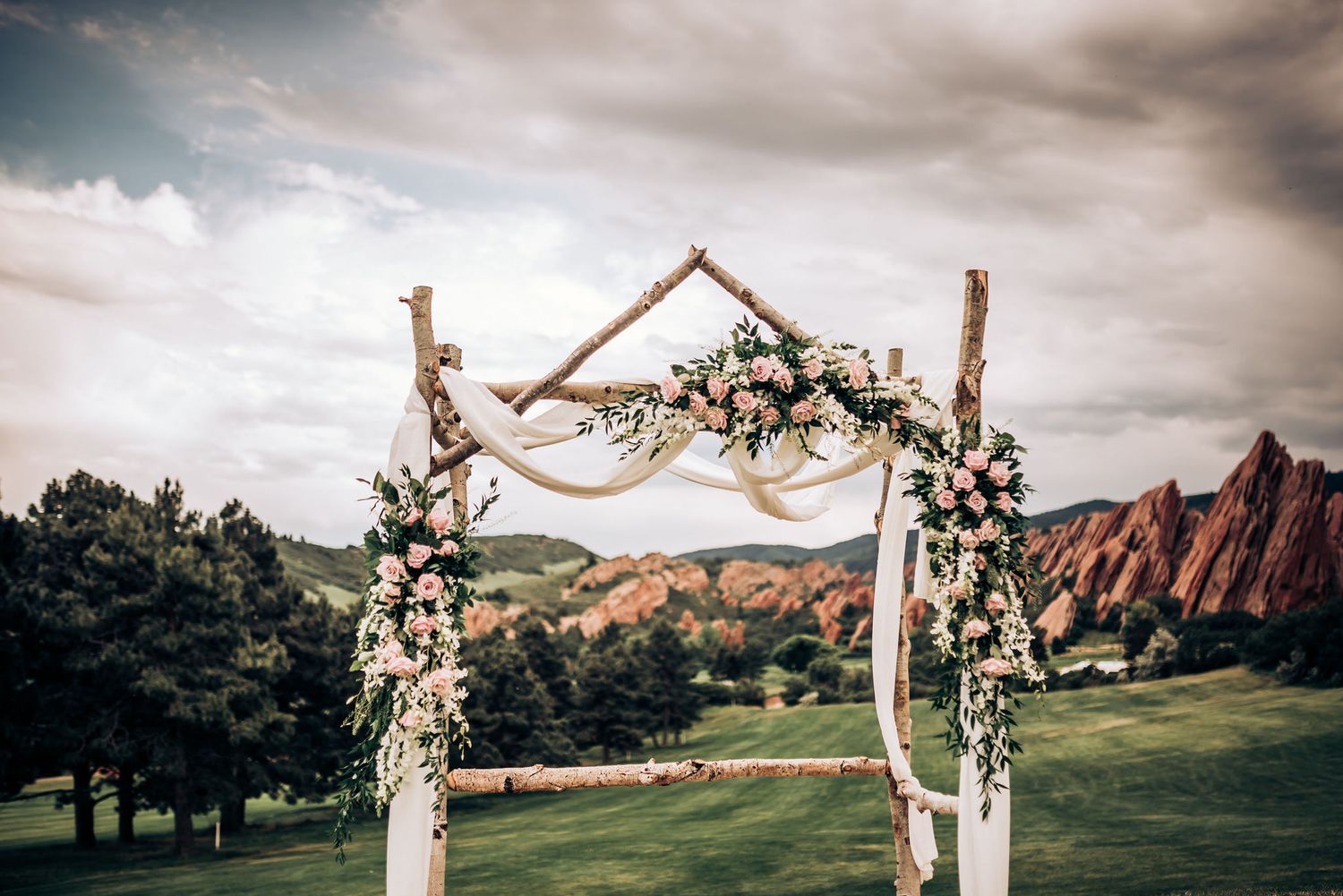 Floral wedding arch with white draping set against red rock mountains.