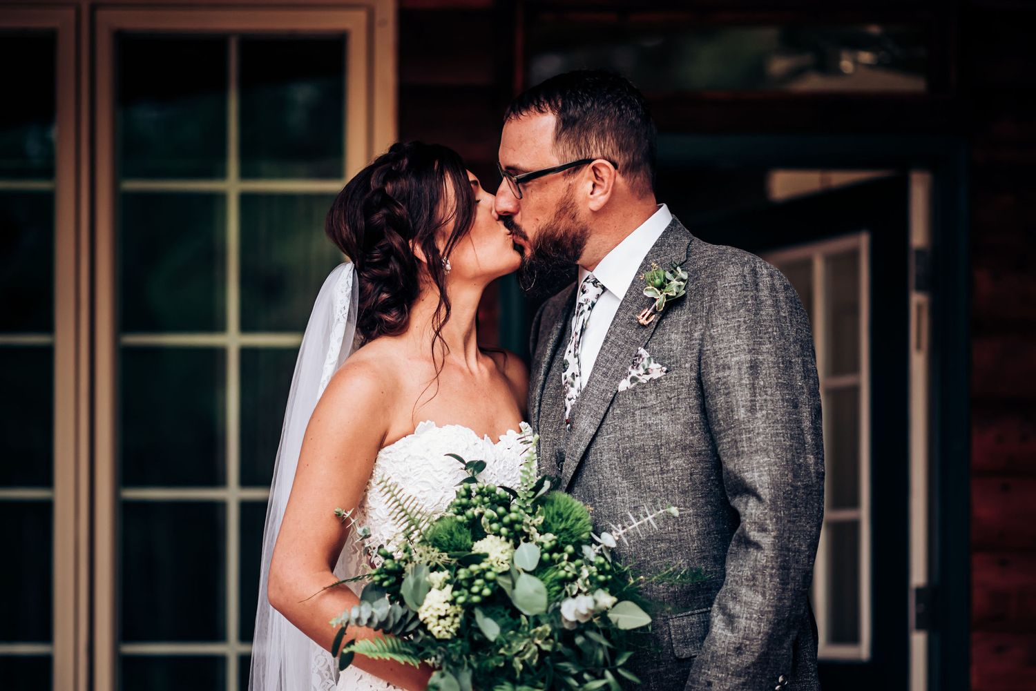 Intimate wedding portrait with bride holding green bouquet while sharing kiss with groom.