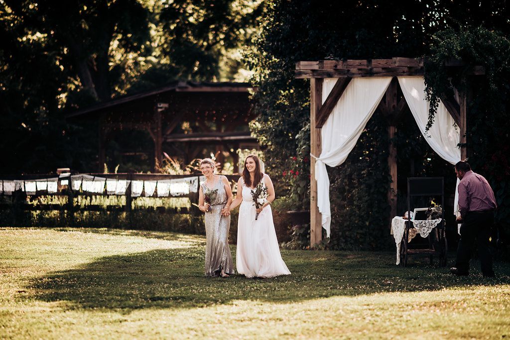 An outdoor wedding ceremony takes place at a rustic venue with white draped arch.