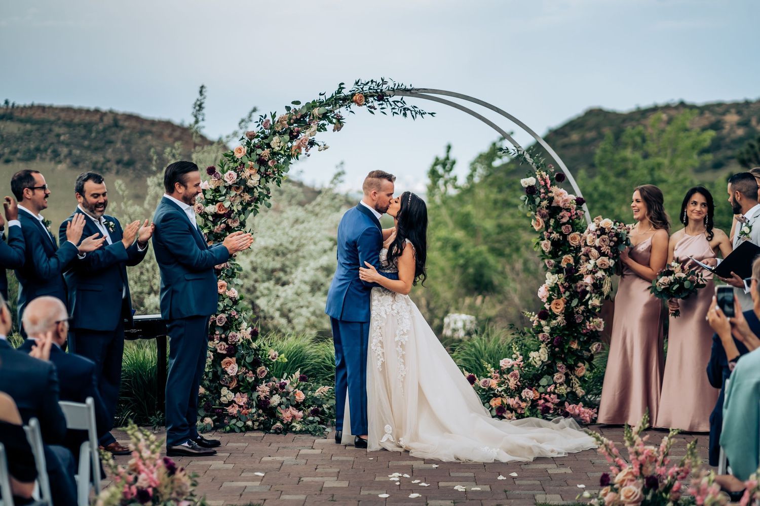 Wedding ceremony under floral arch with mountain landscape backdrop.