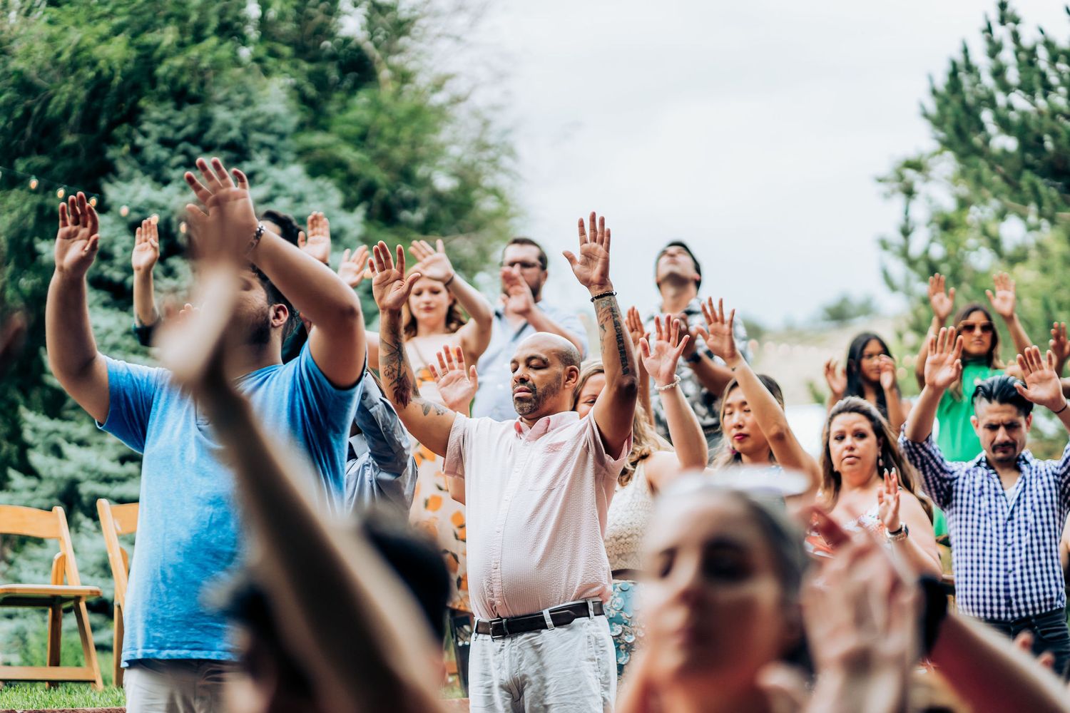 Enthusiastic crowd of wedding guests raising their hands in joy during an outdoor celebration.