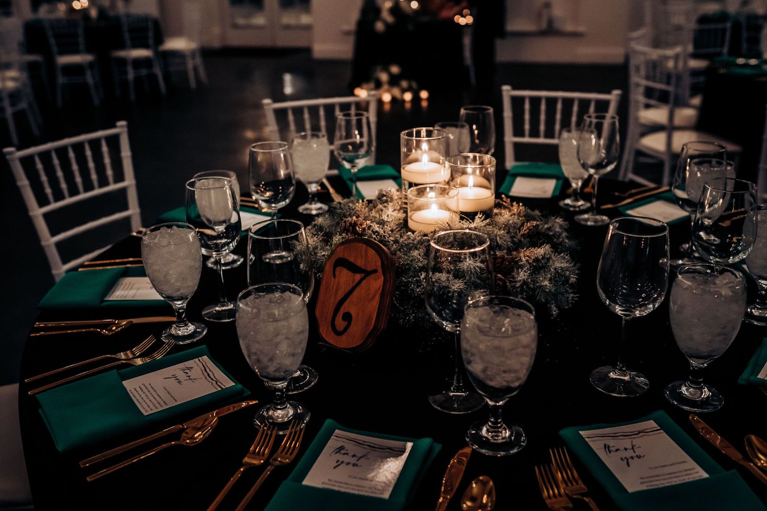 Elegant wedding table setting with candlelight, emerald napkins and gold cutlery.