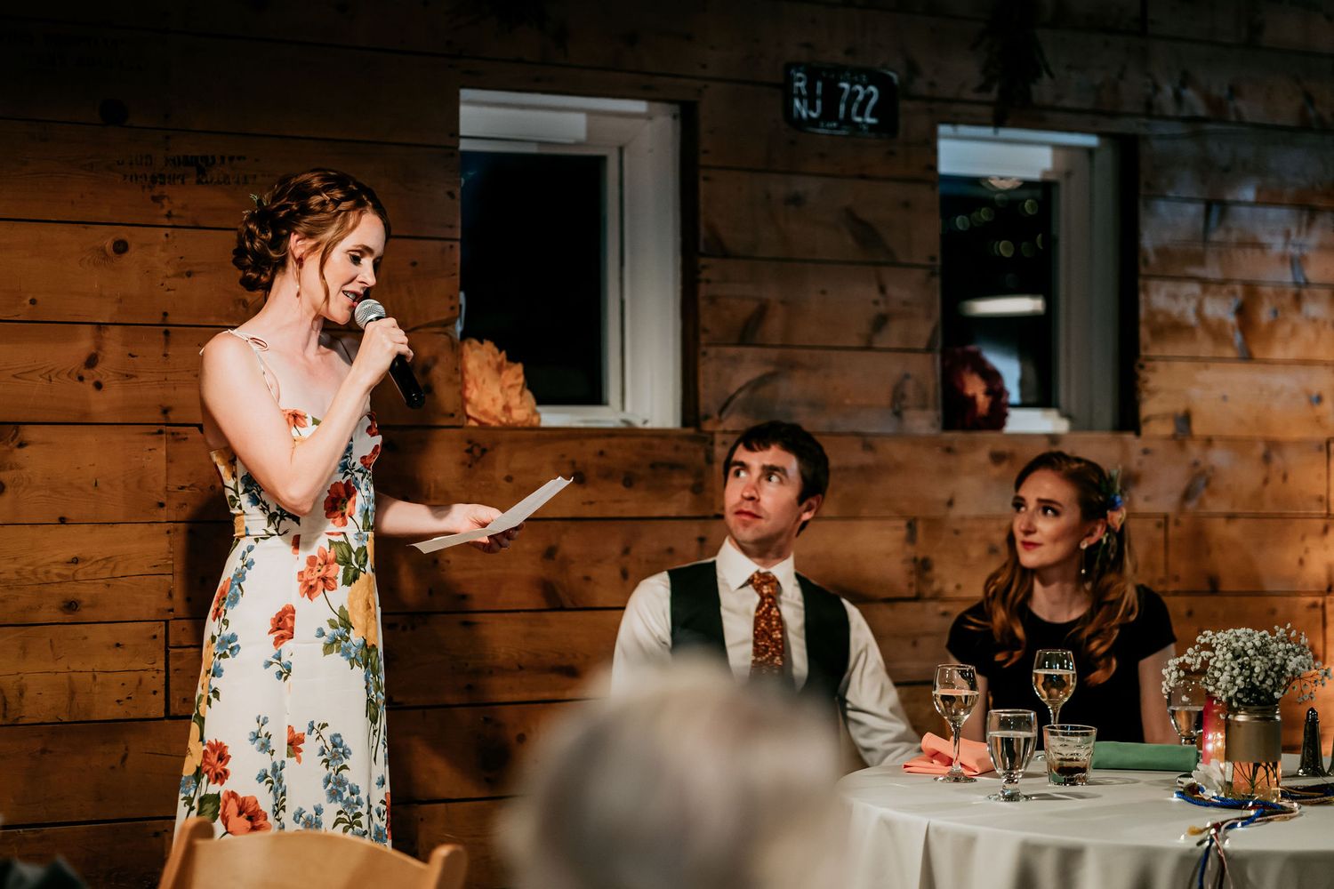 A wedding toast scene inside a rustic wooden venue with guests seated at decorated tables.