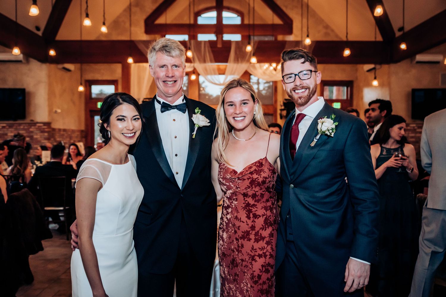 Formal group photo of wedding party members in a rustic wooden venue with exposed beams.