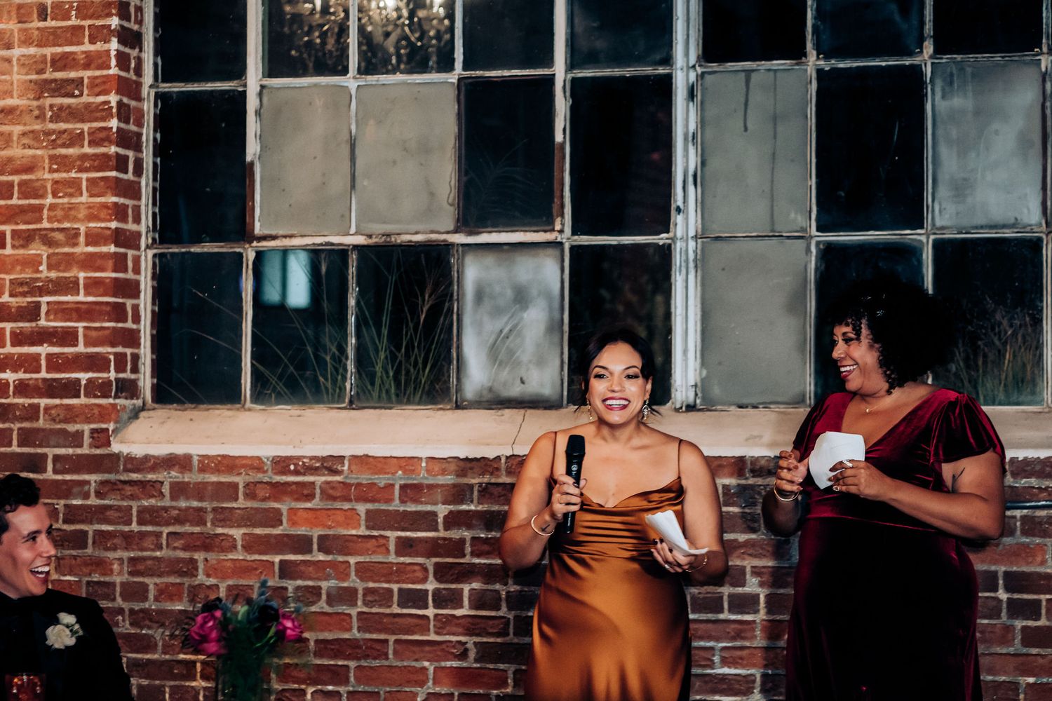 A speech being given during a wedding reception in an industrial brick venue with large windows.