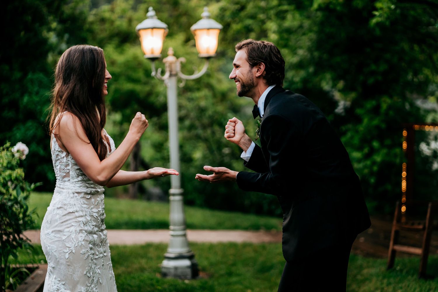 A couple shares an animated conversation under a vintage lamppost during their wedding celebration.