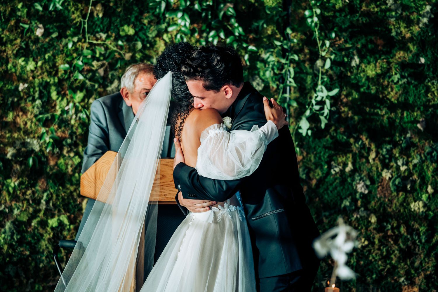 Romantic wedding moment in front of ivy-covered wall with vintage lighting.