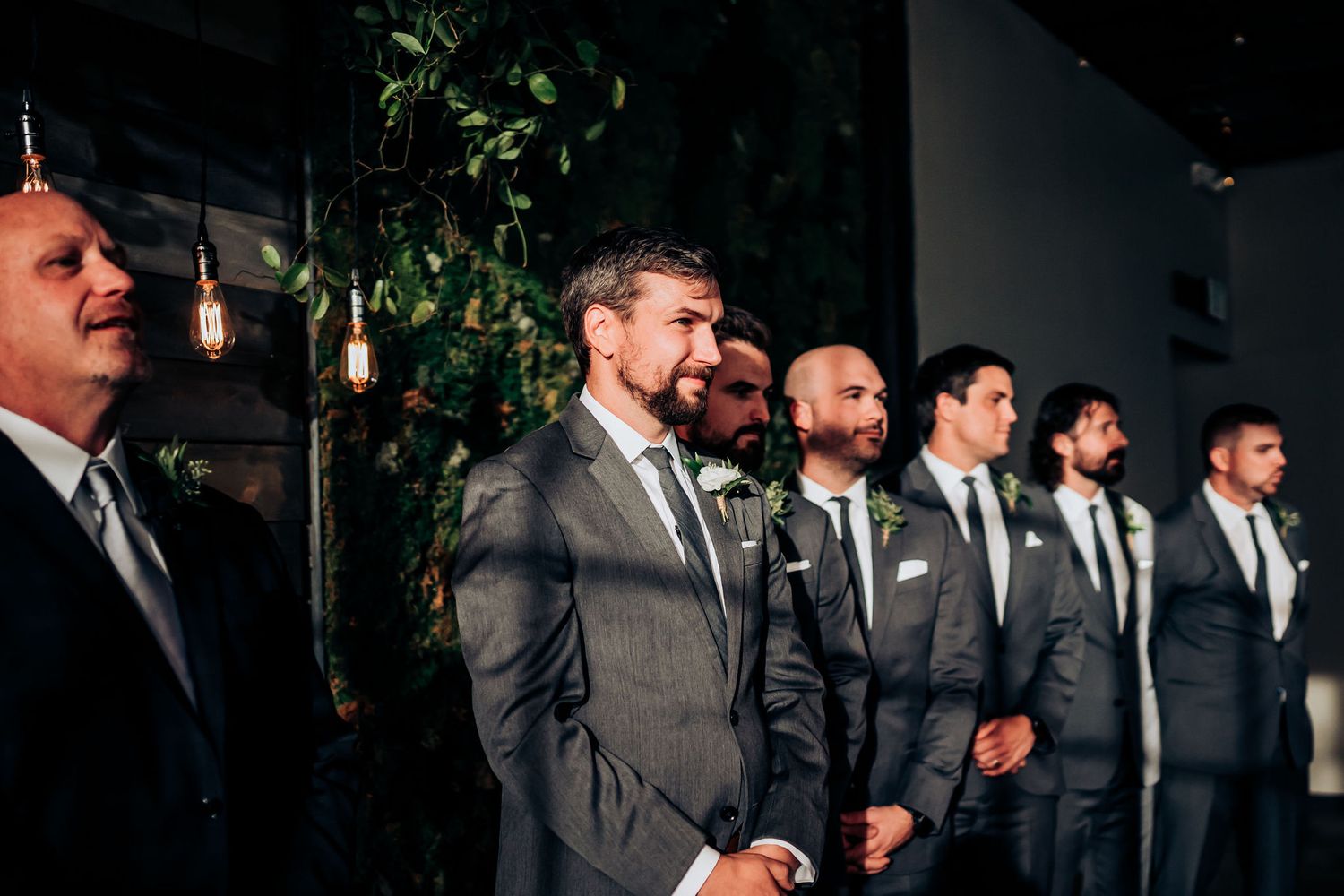 Groomsmen lined up in matching gray suits watching the wedding ceremony.