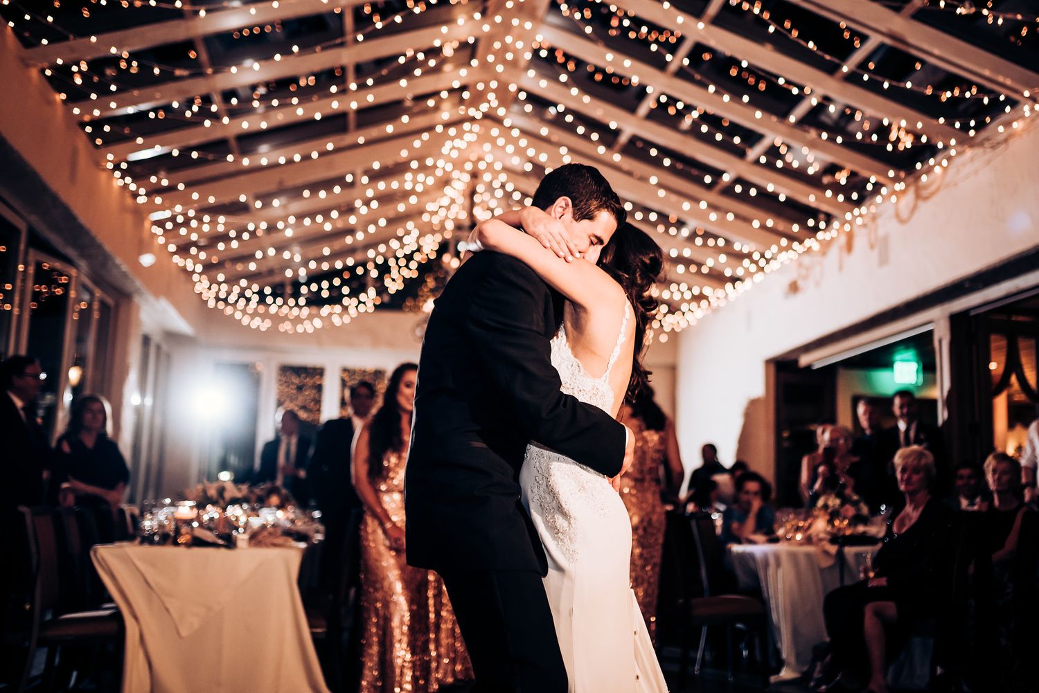 Couple shares romantic dance under canopy of twinkling fairy lights at wedding reception.