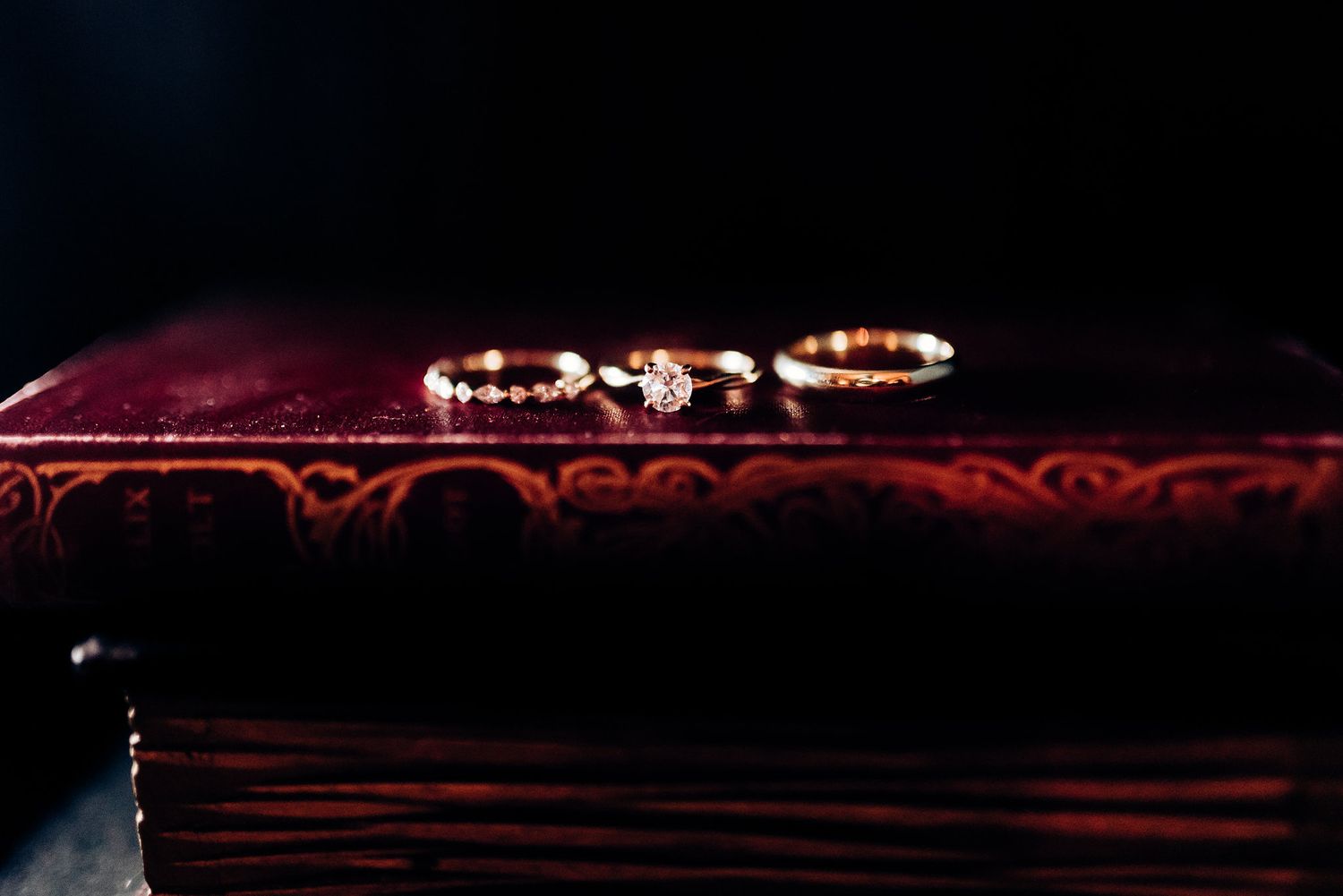 Wedding rings displayed on rich burgundy velvet surface in dramatic lighting.