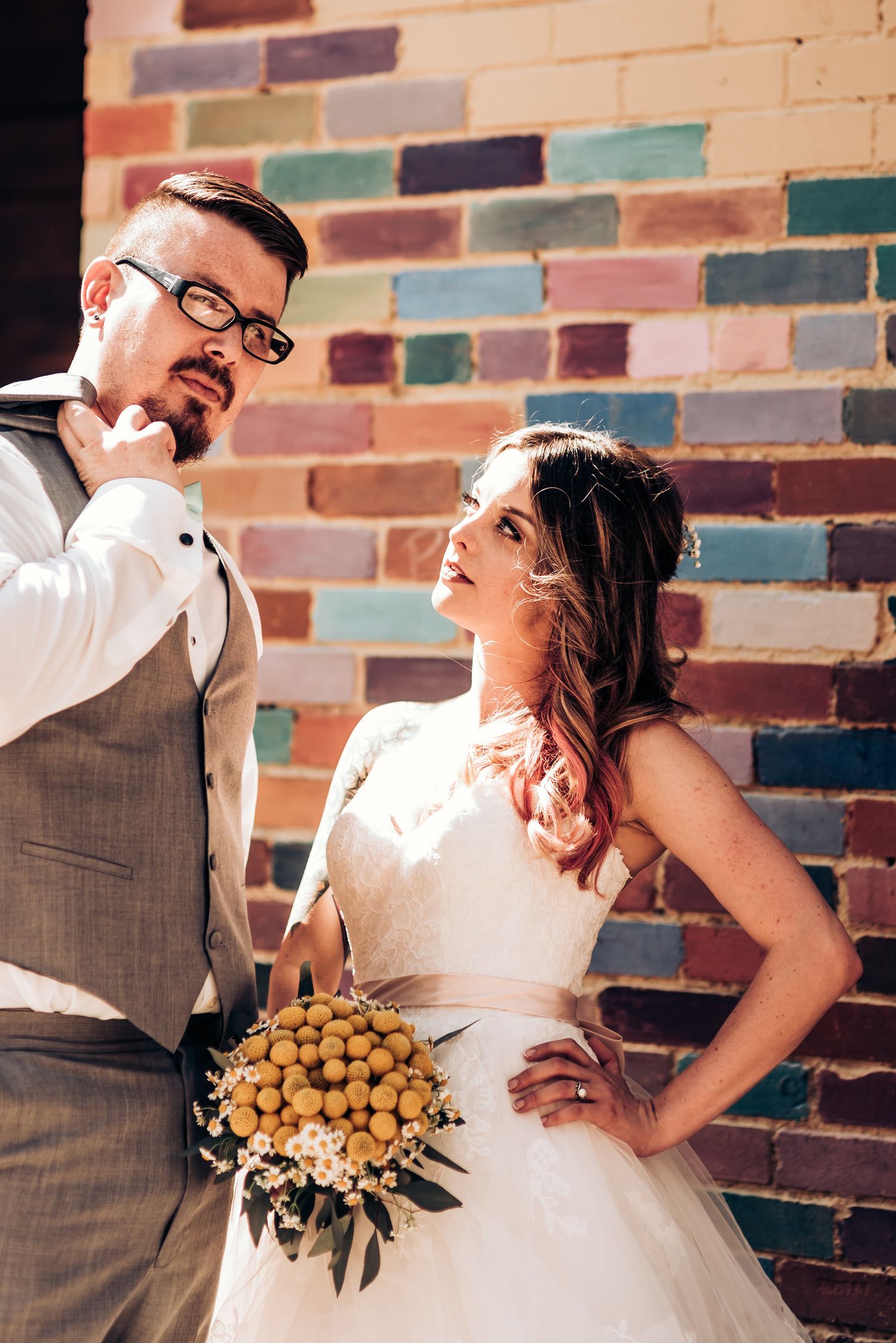 A stylish wedding portrait featuring a yellow bouquet against colorful brick.