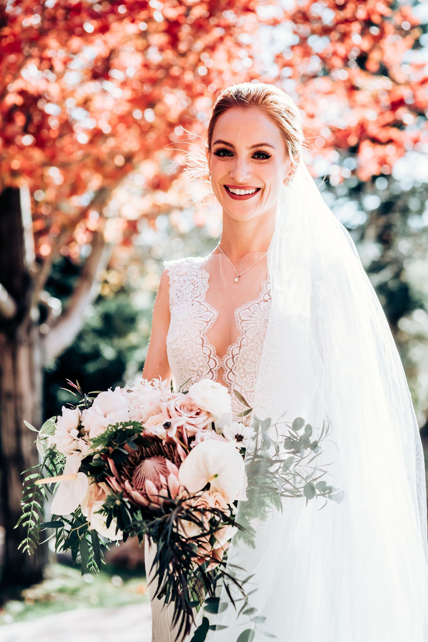 Stunning bridal portrait showcasing a lace wedding gown and elegant bouquet under autumn trees.