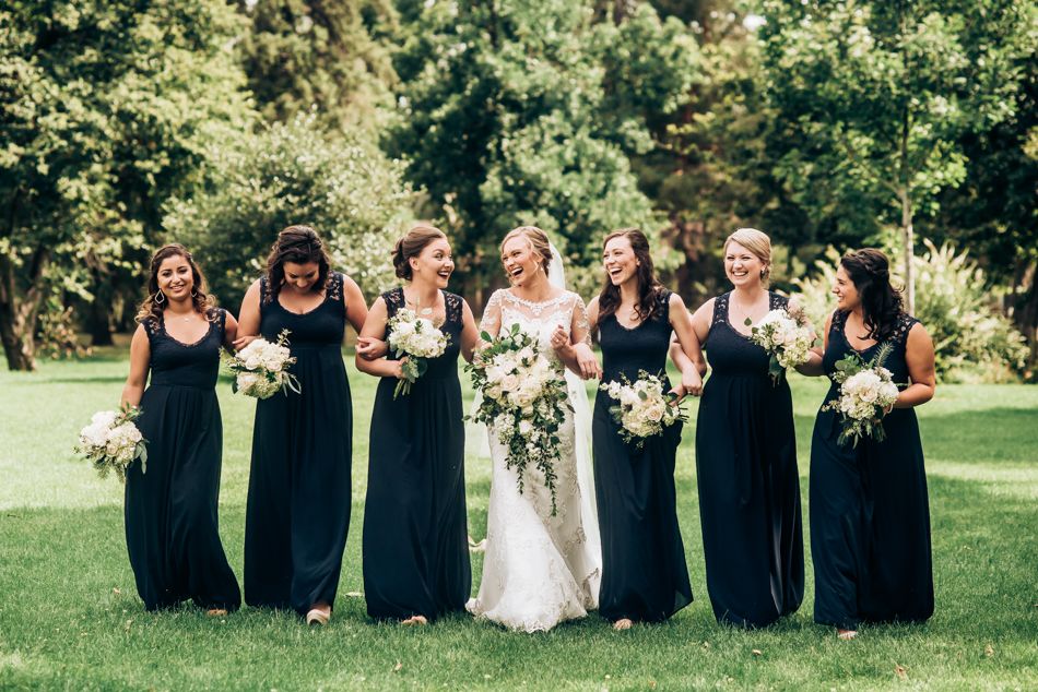 Wedding party poses outdoors with bridesmaids in navy dresses holding white floral bouquets.