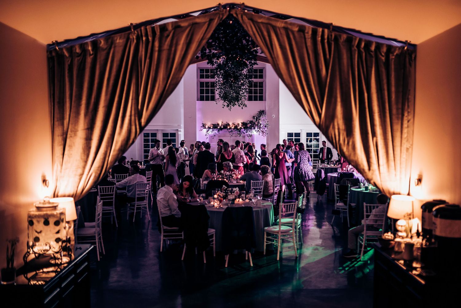 Dramatic evening reception venue with draped curtains and ambient lighting creating a romantic atmosphere.