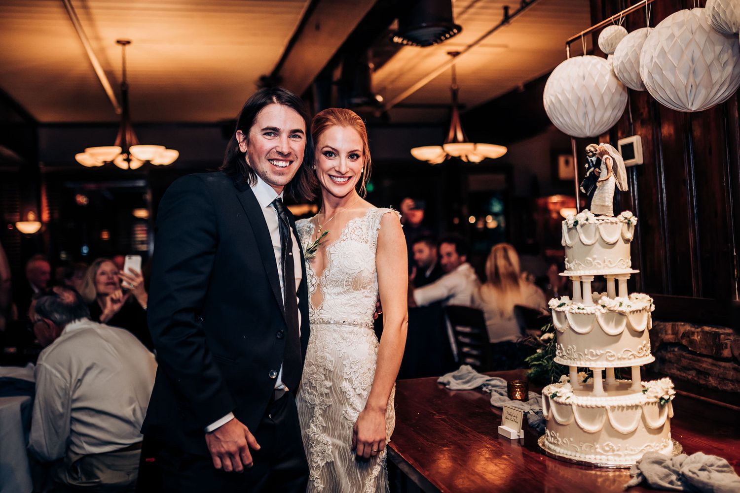 Couple poses next to their elegant tiered white wedding cake during their reception celebration.