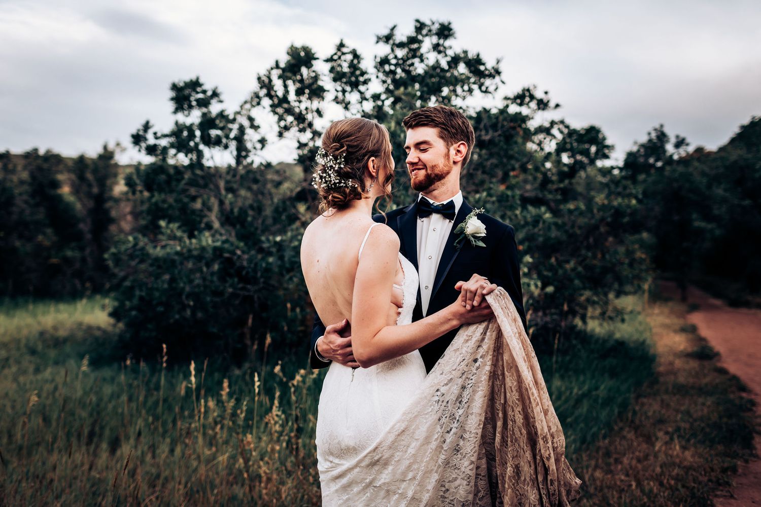 Romantic wedding couple embraces on a nature trail surrounded by trees at dusk.