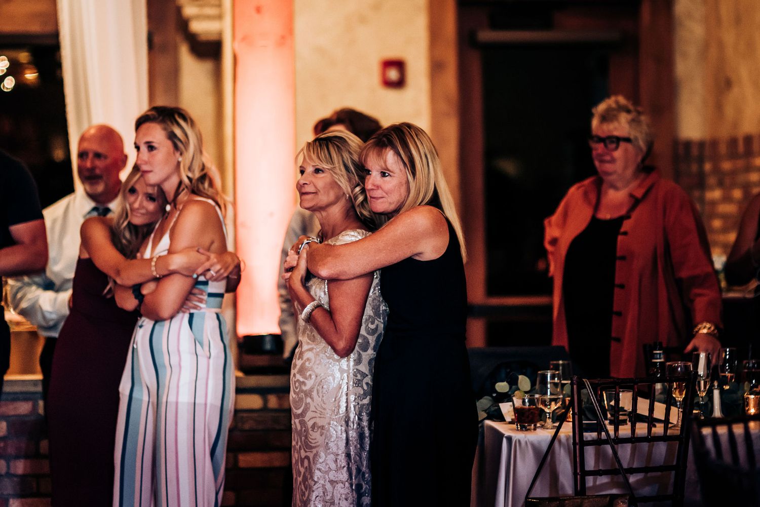 Emotional wedding guests embrace while watching the reception festivities.