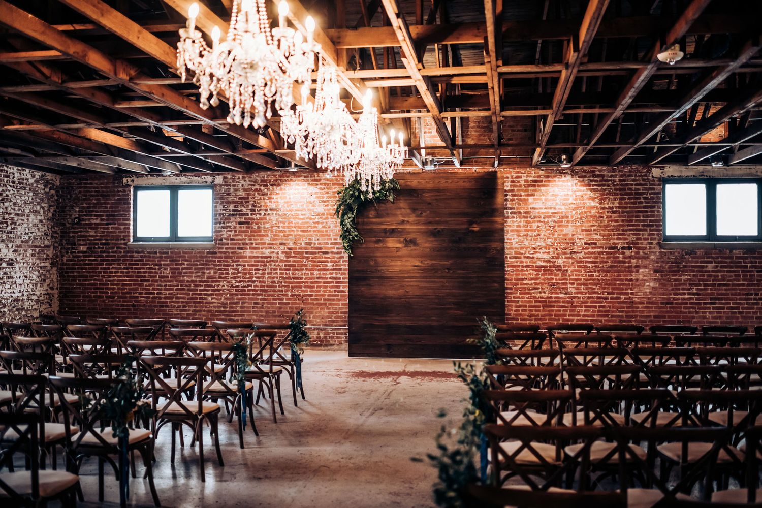 A romantic wedding venue with crystal chandeliers and exposed brick walls lined with wooden chairs.