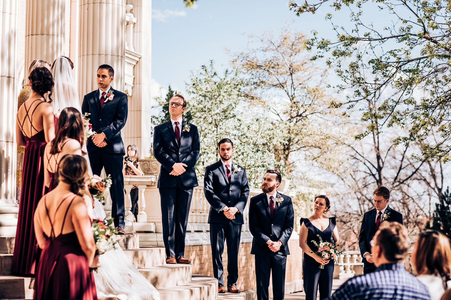 Wedding party standing on columned steps during an outdoor ceremony.