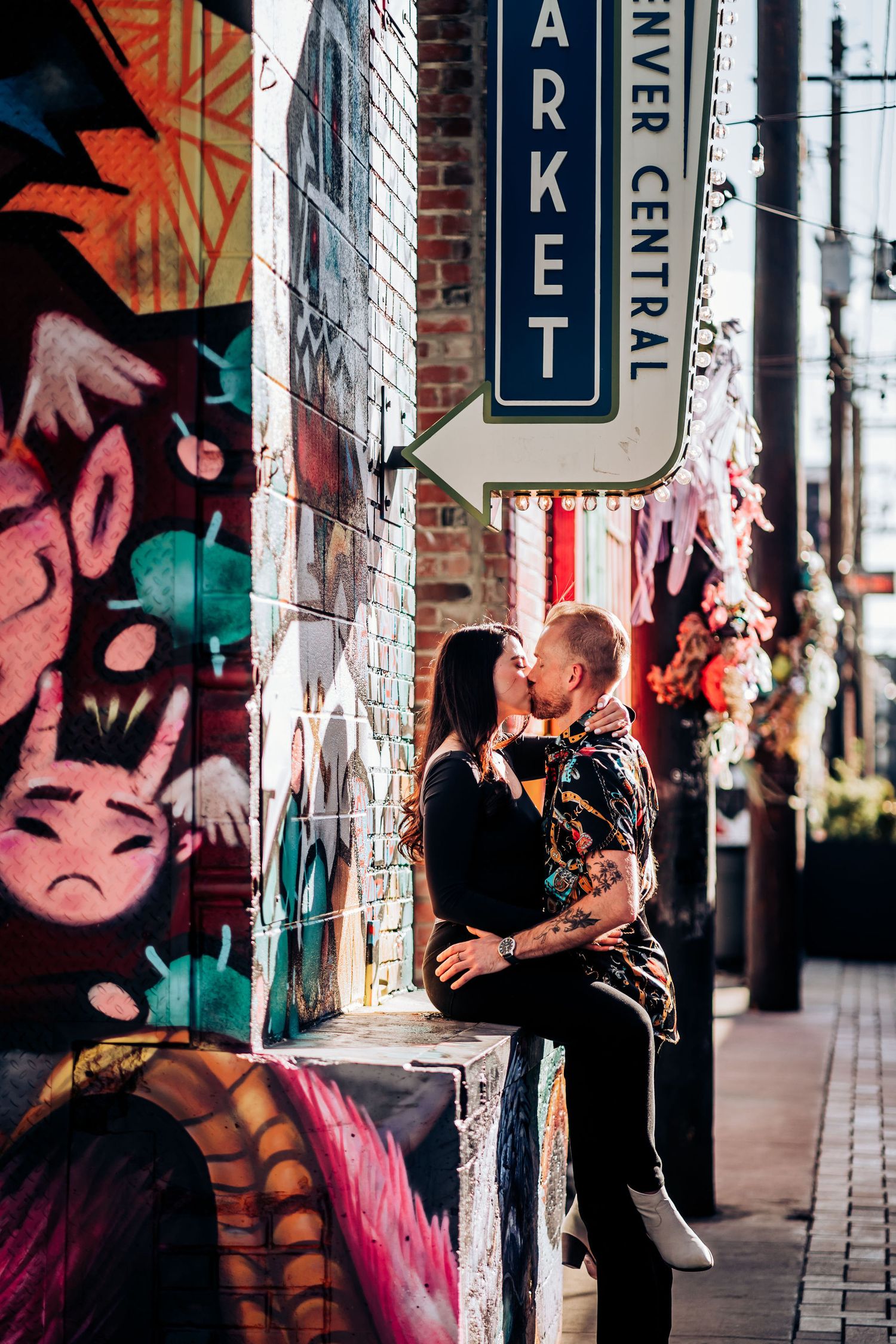 A couple embracing under a market sign with vibrant street art and brick walls.