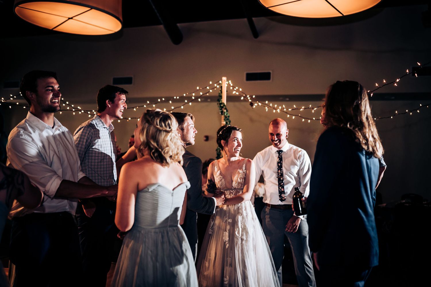 Group of wedding guests dancing and celebrating under ambient lighting and string lights.