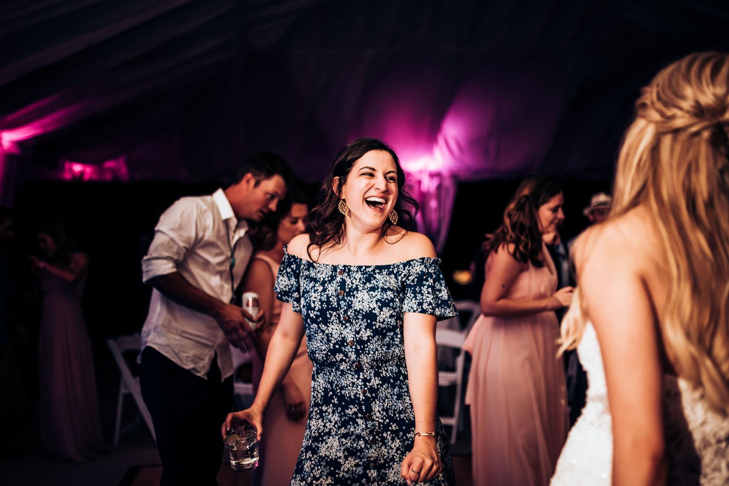 Guests enjoying themselves on the dance floor at a wedding reception with pink mood lighting.