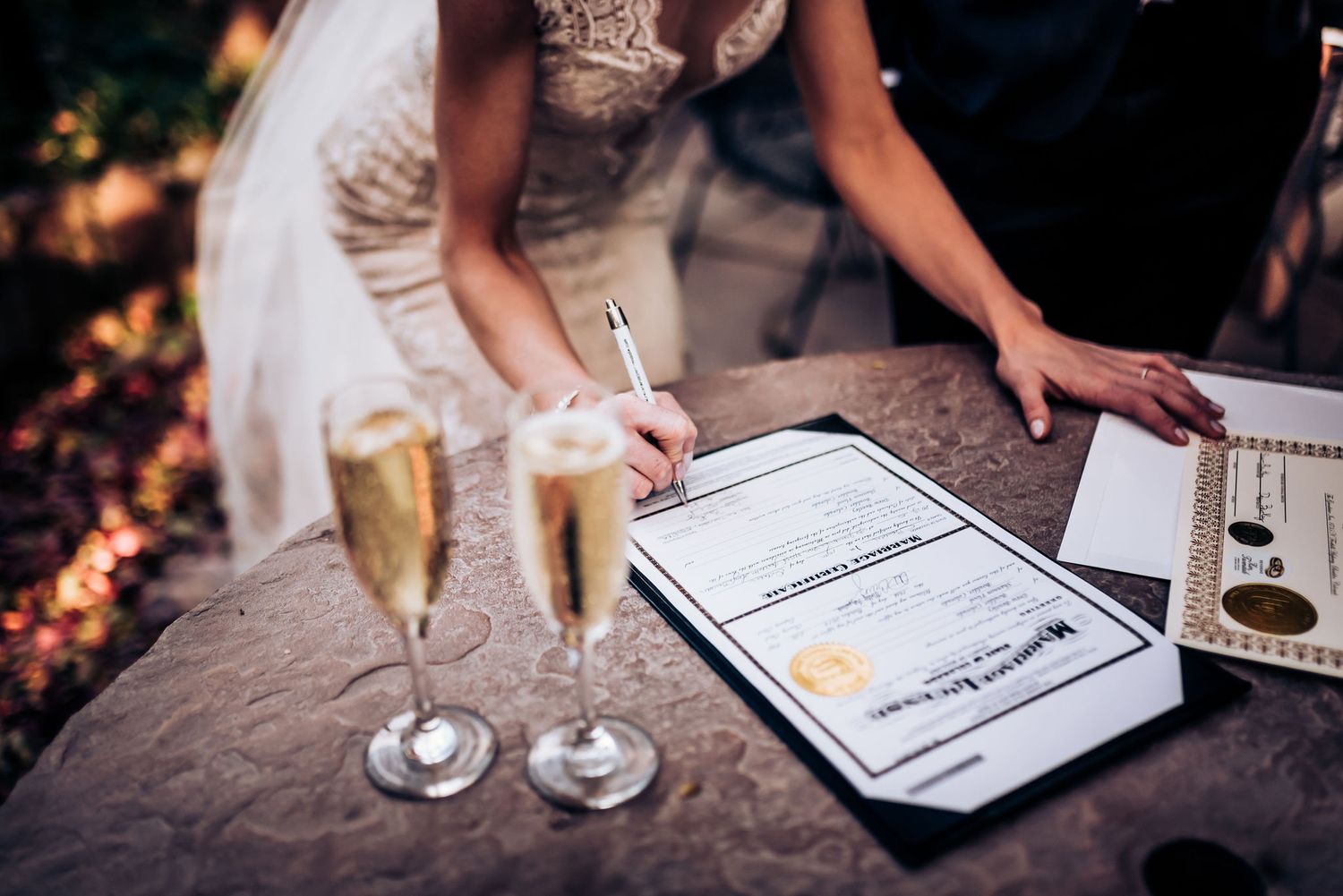 Wedding documents being signed with champagne glasses on textured tablecloth during sunset.