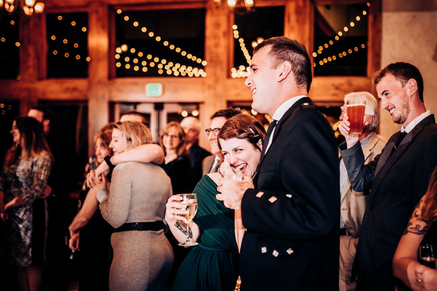 Wedding guests in formal attire enjoy reception under string lights.