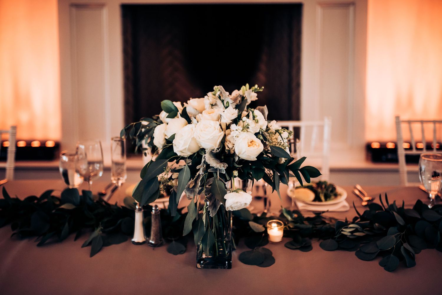 Elegant white floral centerpiece with greenery on dark tablecloth.