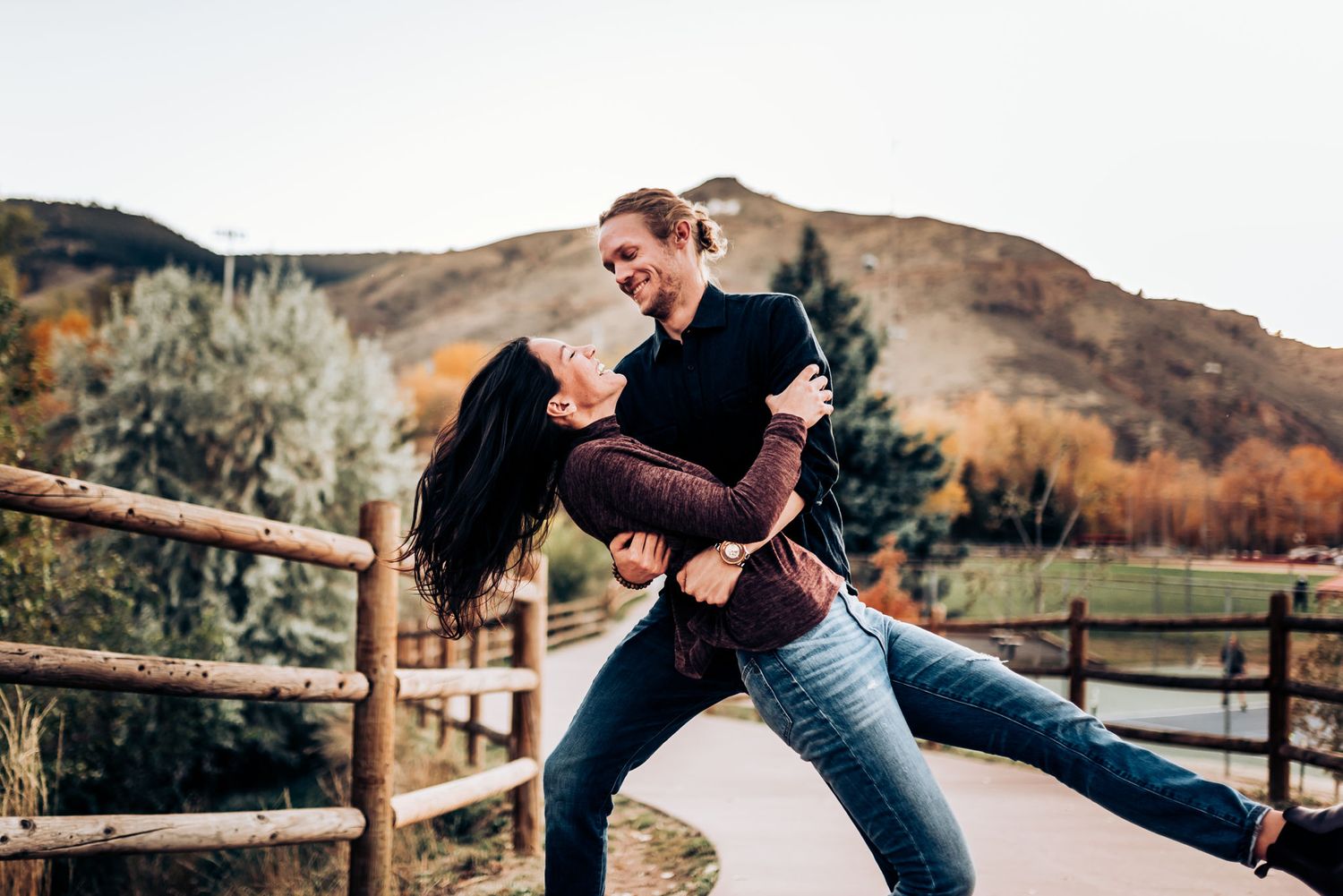 A romantic dip pose between a couple against a backdrop of fall mountains and wooden fencing.