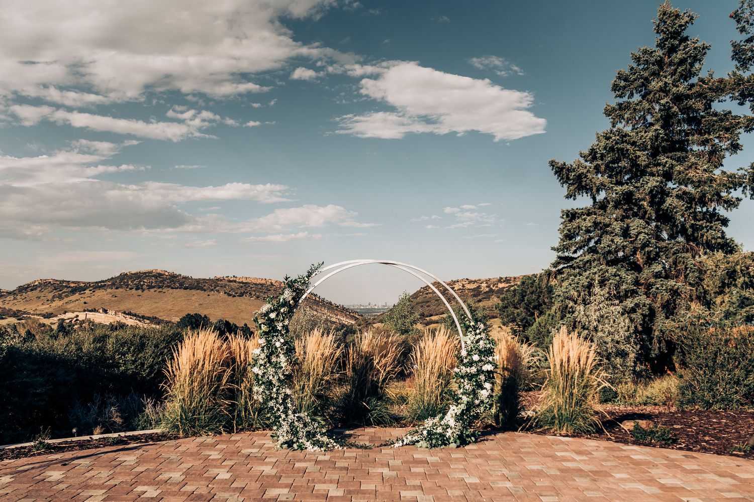 A scenic mountain wedding venue with an arch decorated in greenery against a blue sky backdrop.