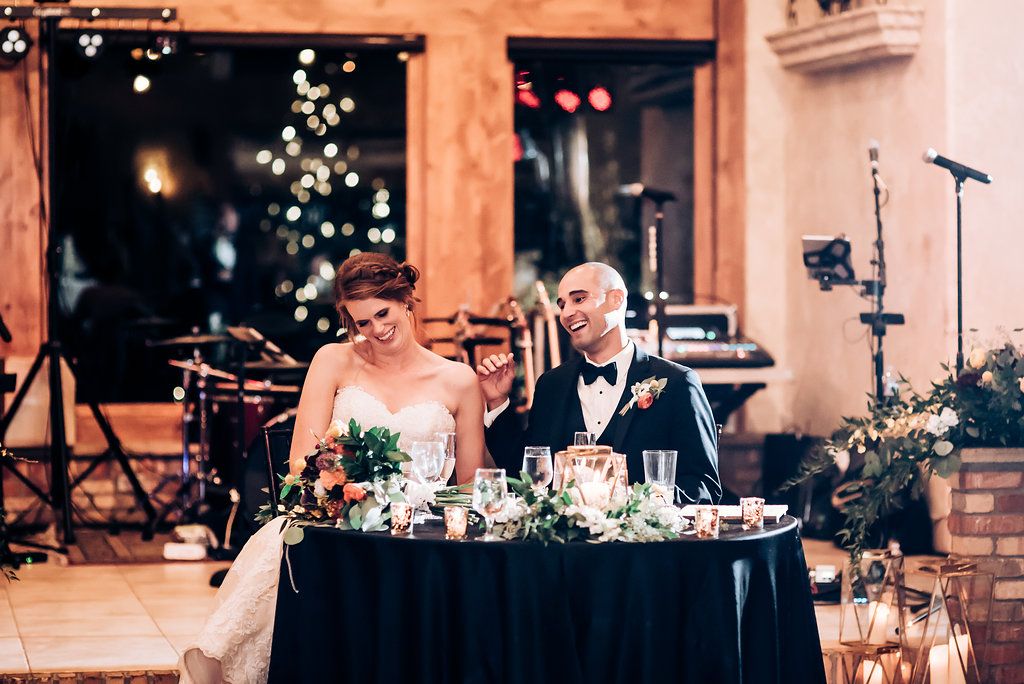 Couple sits at an elegant reception table with romantic lighting and floral centerpieces.