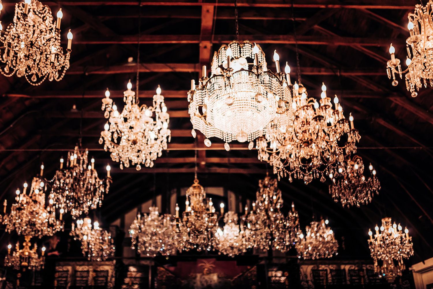 Multiple crystal chandeliers hanging from a rustic wooden beam ceiling create an elegant atmosphere.