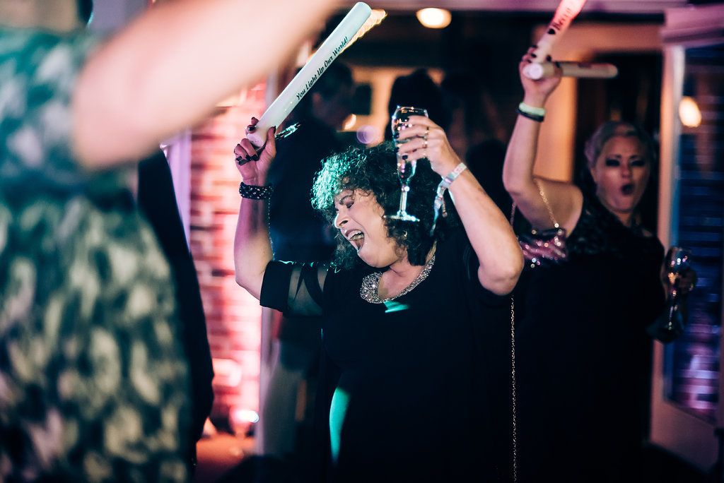 Lively dance party celebration with guests raising drinks under colored lighting.