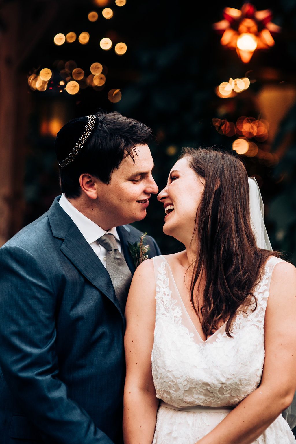 Joyful wedding couple laughing together under glowing bokeh lights at dusk.