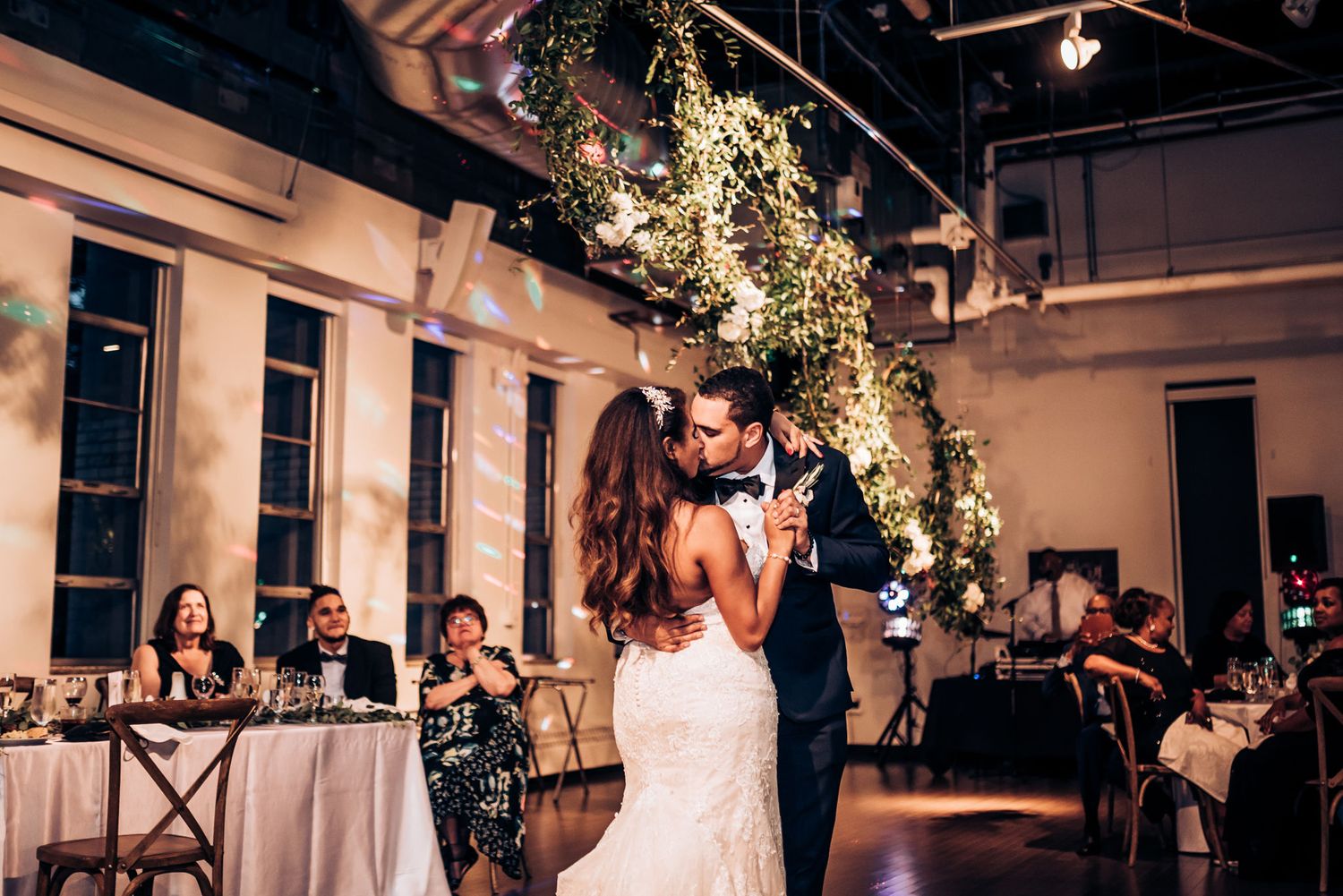 Newlyweds share an intimate slow dance beneath hanging greenery and floral decorations.