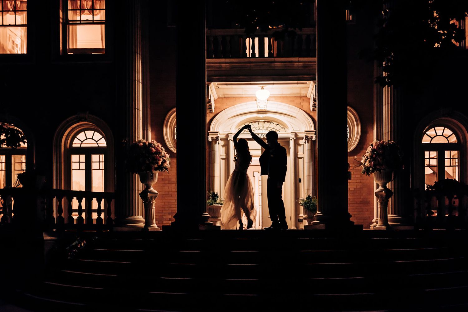 A silhouetted couple stands in an illuminated archway of a grand building at night.