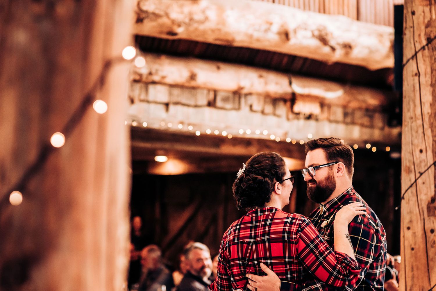 Two people sharing an intimate dance moment in a rustic barn with string lights.
