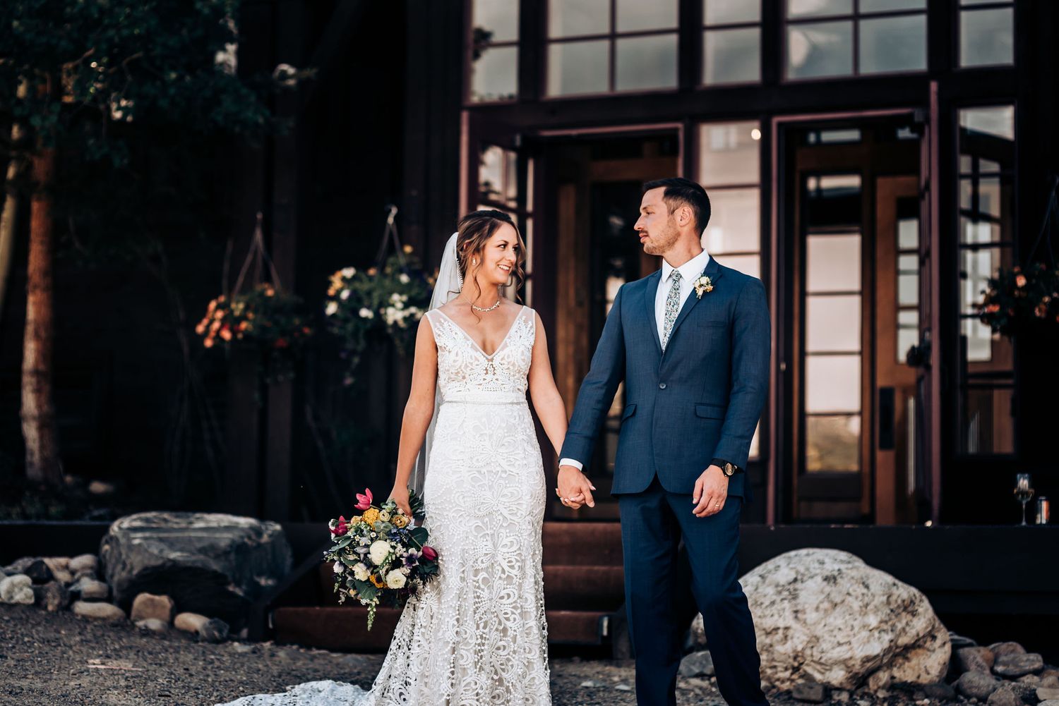 Elegant wedding portrait outside mountain venue with bride in lace gown.