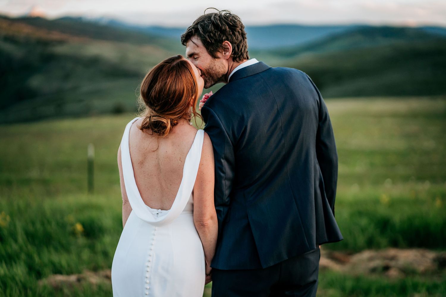 A romantic moment between newlyweds against a backdrop of scenic mountain landscapes at sunset.
