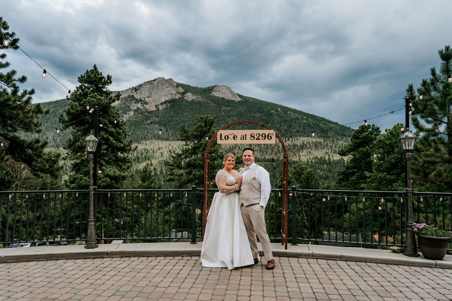 A couple poses for a wedding portrait on a mountain overlook deck with scenic peaks in background.