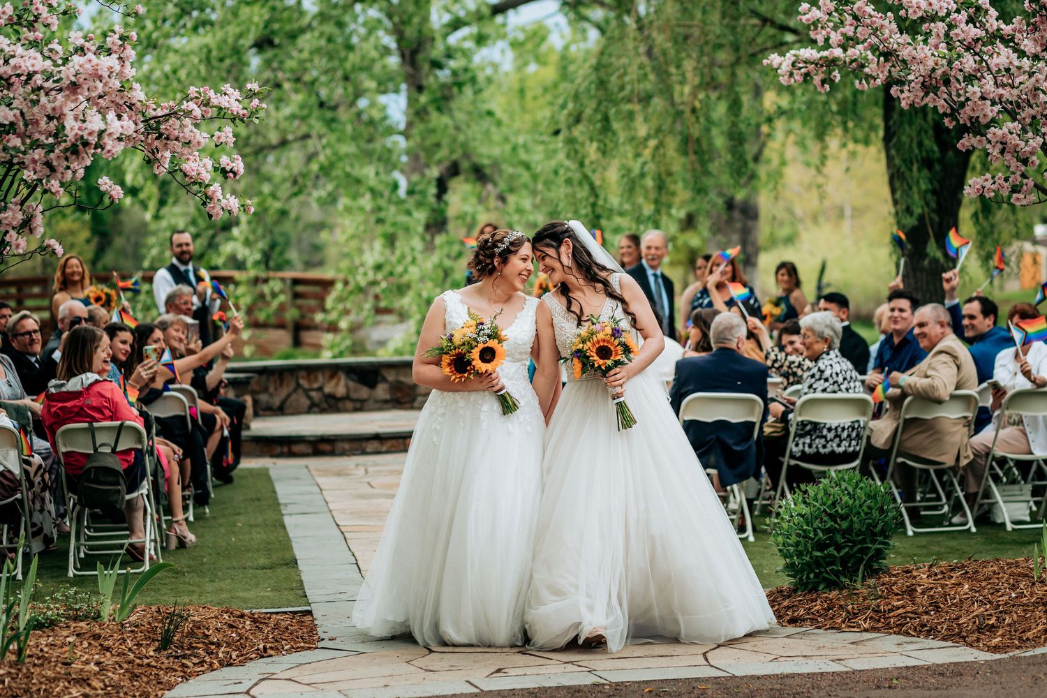 Wedding couple walking down aisle under cherry blossoms as guests celebrate with flower petals.