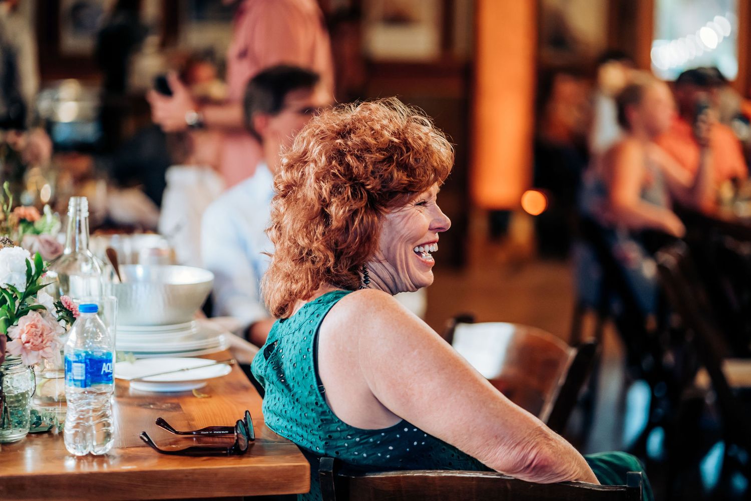 Guest wearing teal dress smiles during wedding reception at indoor venue.