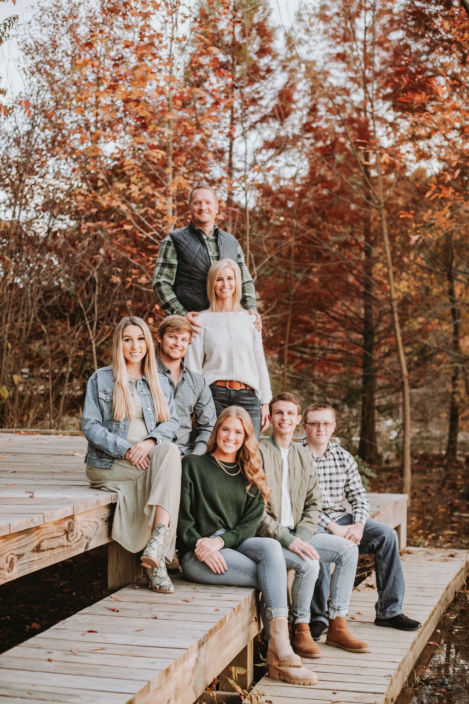 A group sits casually on wooden deck steps surrounded by autumn trees with orange and red foliage in the background.