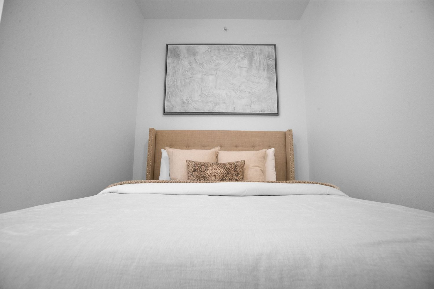 Minimalist bedroom with white bedding and gray artwork above headboard.