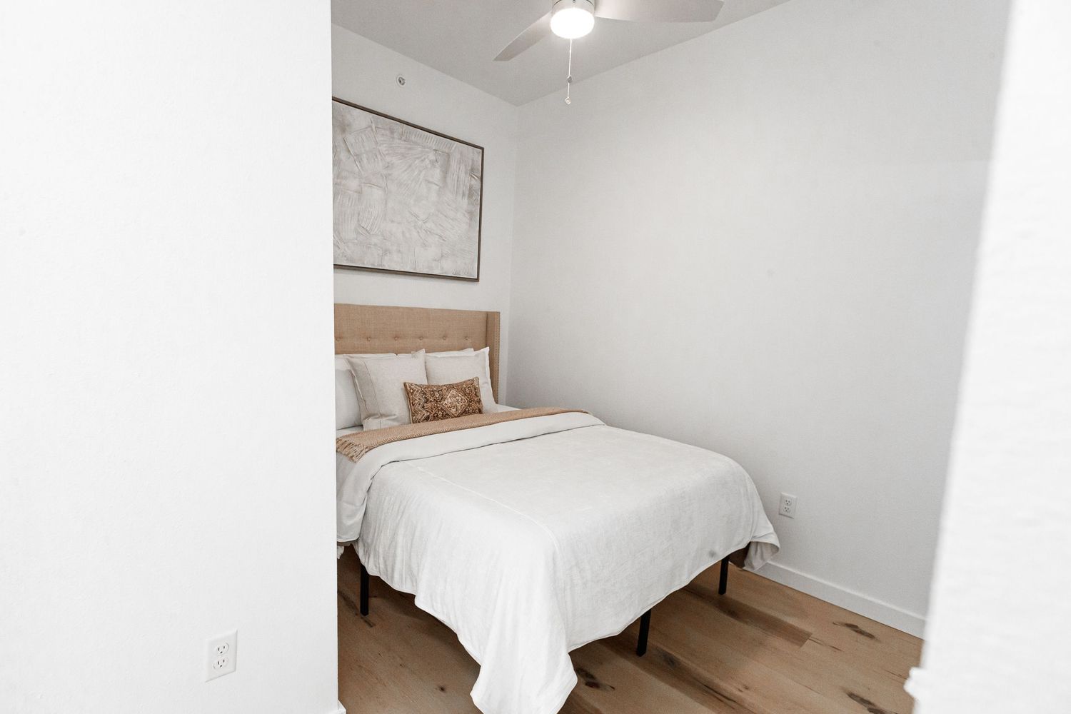 Clean white bedroom with wooden headboard, white bedding, and simple wall decor.